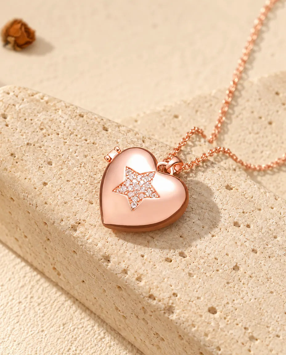 Collar relicario de corazón con estrella de circonitas en color oro rosa sobre travertino, con luz cálida de sol
