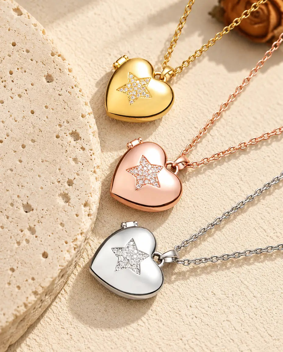 Relicarios de corazón con estrella de circonitas dorado, color oro rosa y plateado apilados junto a una losa de travertino