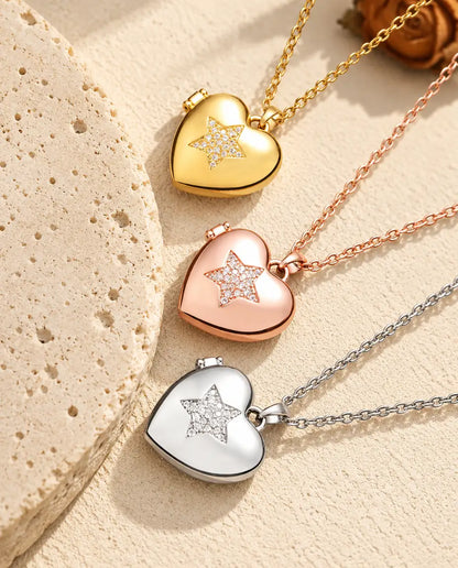 Relicarios de corazón con estrella de circonitas dorado, color oro rosa y plateado apilados junto a una losa de travertino