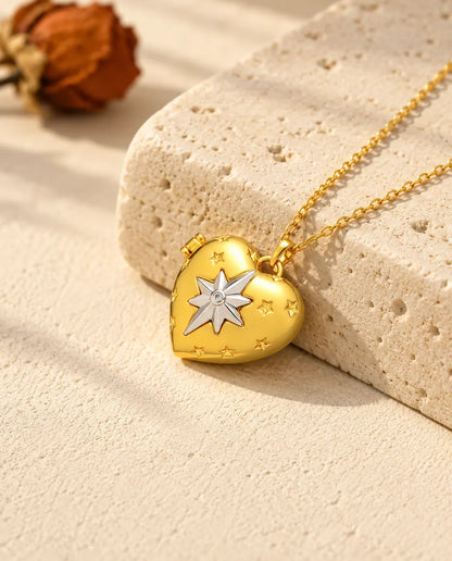 Collar relicario de corazón dorado con la estrella polar plateada, apoyado en un bloque de travertino