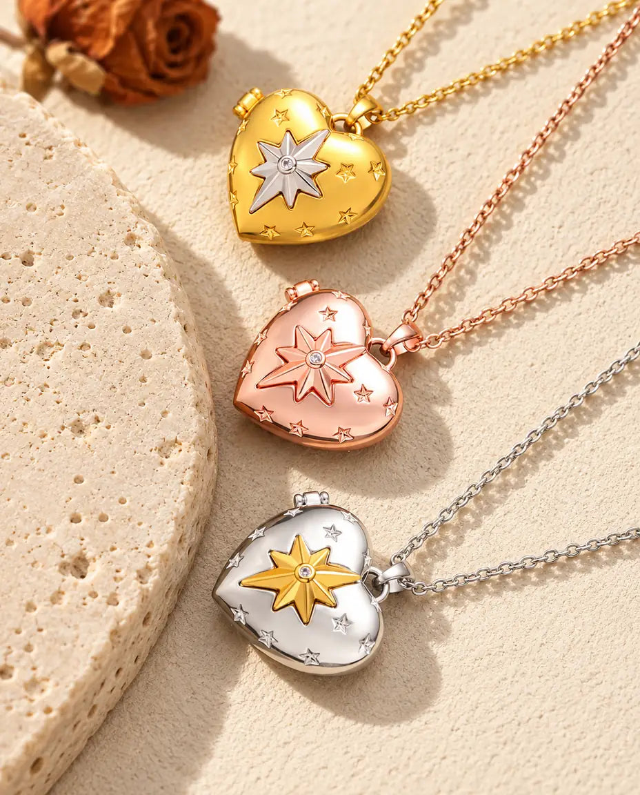 Relicarios de corazón con estrella polar dorado, color oro rosa y plateado apilados junto a una losa de travertino