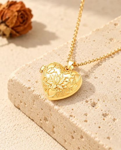 Collar relicario de corazón dorado con flor de loto apoyado sobre un bloque de travertino