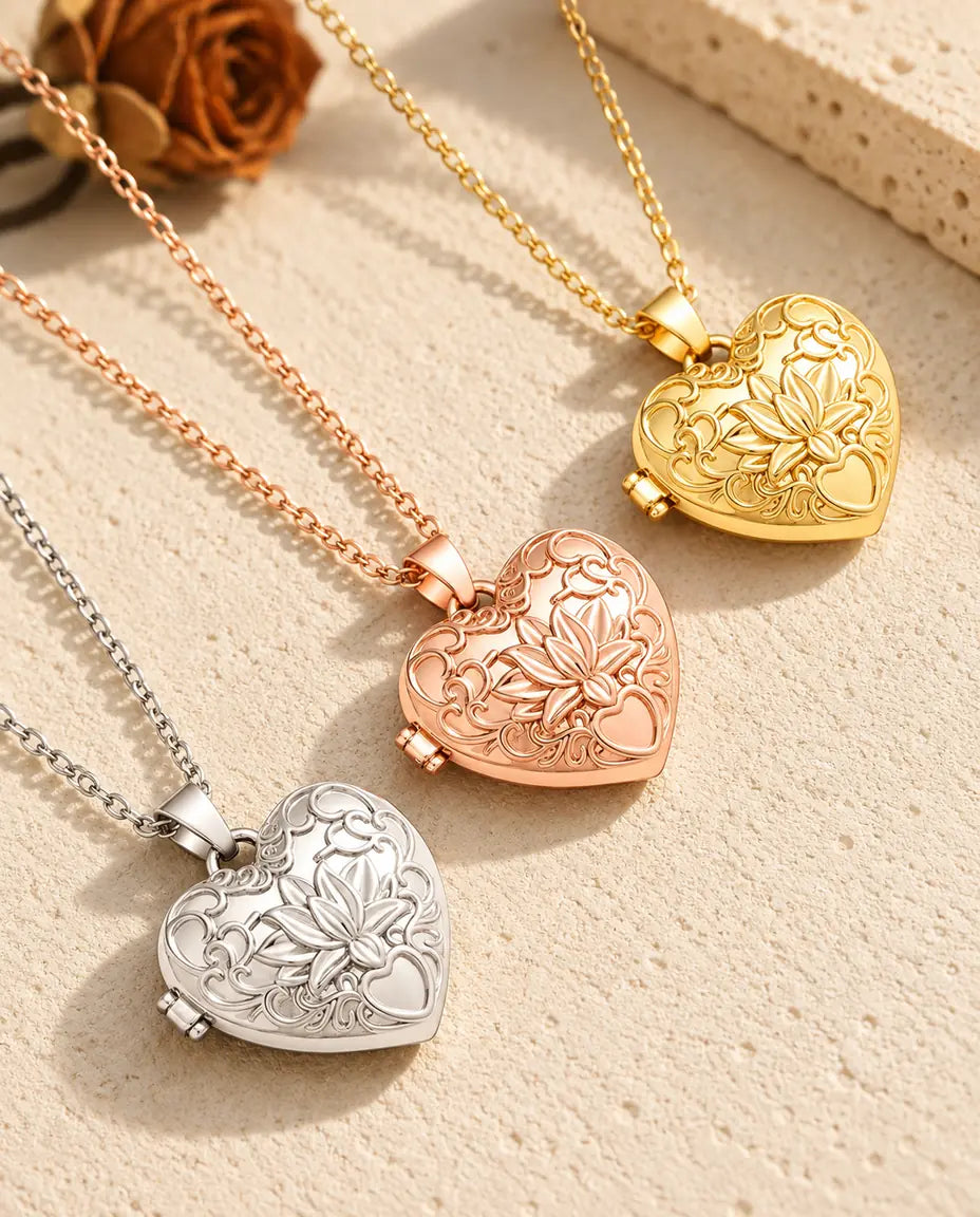 Tres relicarios de corazón con flor de loto, plateado, color oro rosa y dorado, colocados en diagonal sobre yeso crema