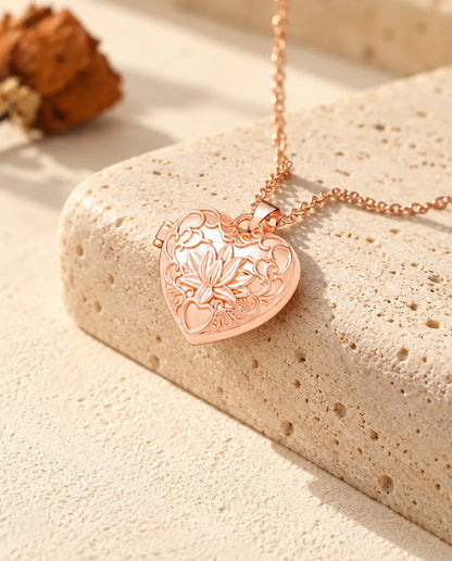 Collar relicario de corazón color oro rosa con flor de loto sobre travertino con luz cálida de sol