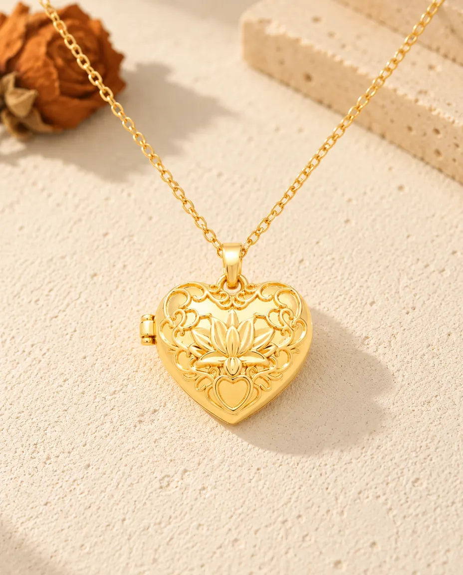 Vista frontal del relicario de corazón dorado con la flor de loto, las volutas y la bisagra lateral