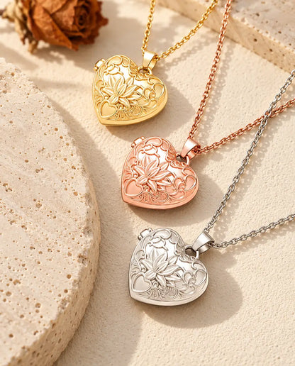 Relicarios de corazón con flor de loto dorado, color oro rosa y plateado apilados junto a una losa de travertino