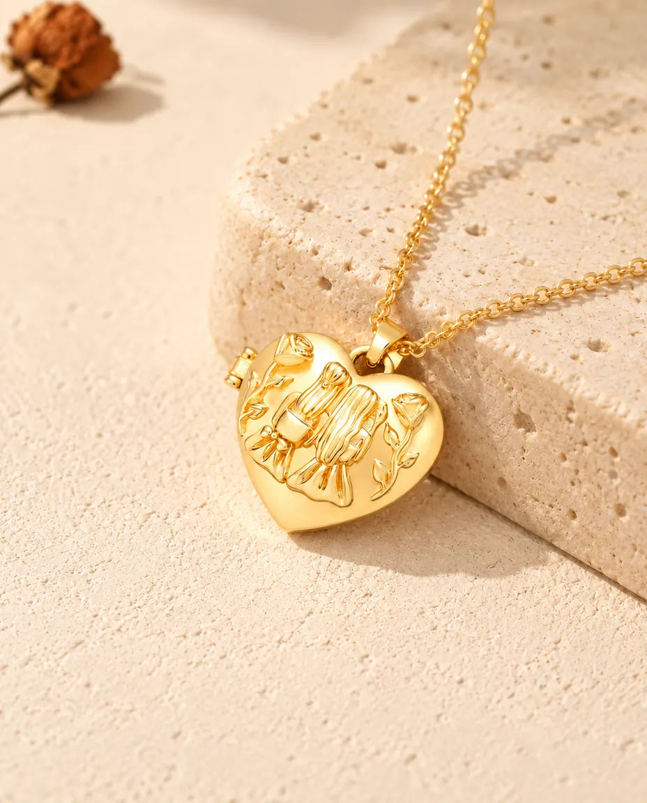 Collar relicario de corazón dorado con dos hermanas y rosas apoyado sobre un bloque de travertino