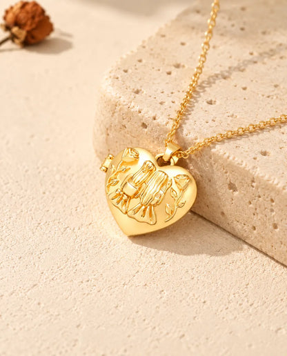 Collar relicario de corazón dorado con dos hermanas y rosas apoyado sobre un bloque de travertino
