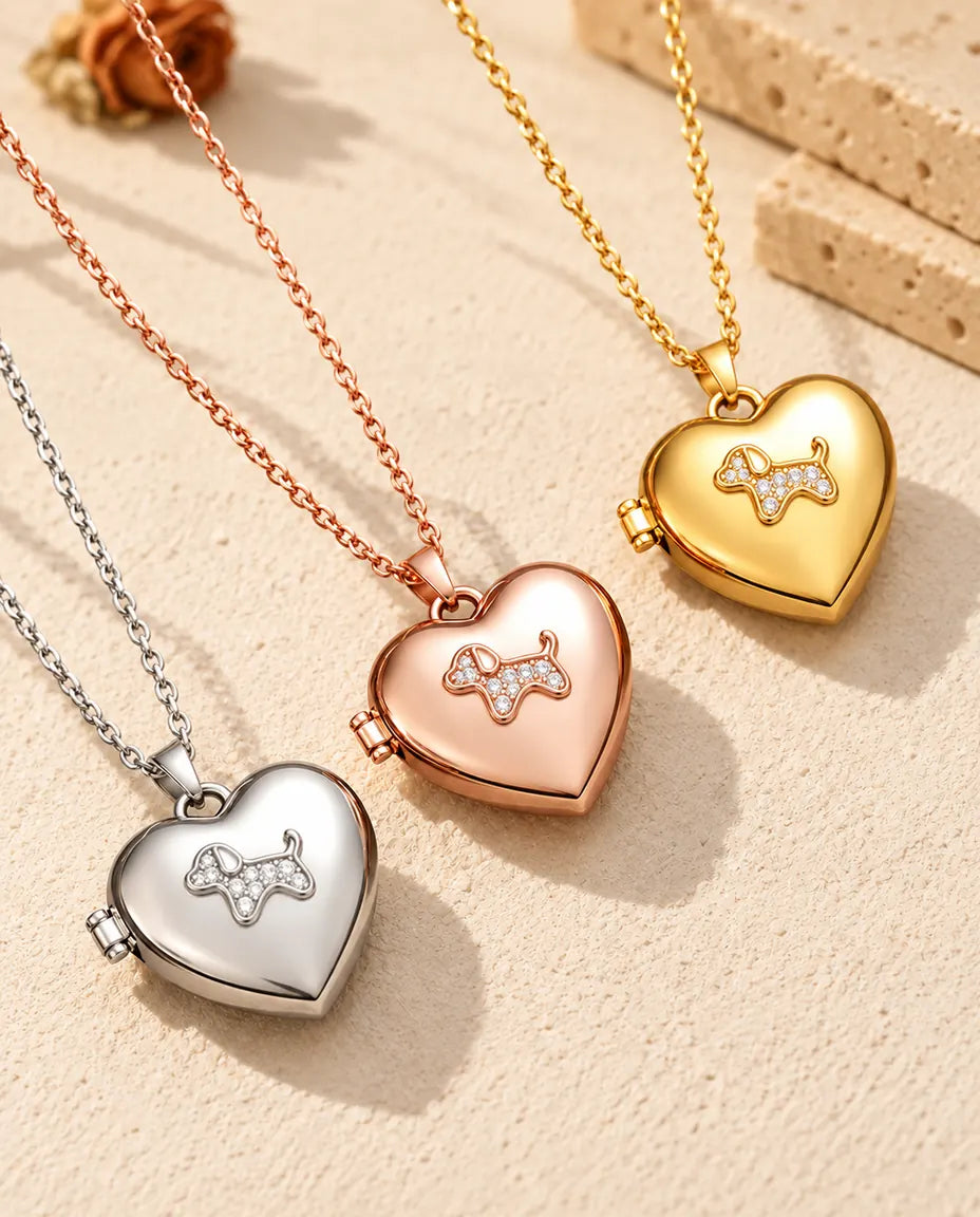 Relicarios de corazón con perrito en plateado, color oro rosa y dorado, colocados en diagonal sobre yeso crema