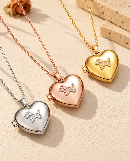 Relicarios de corazón con perrito en plateado, color oro rosa y dorado, colocados en diagonal sobre yeso crema