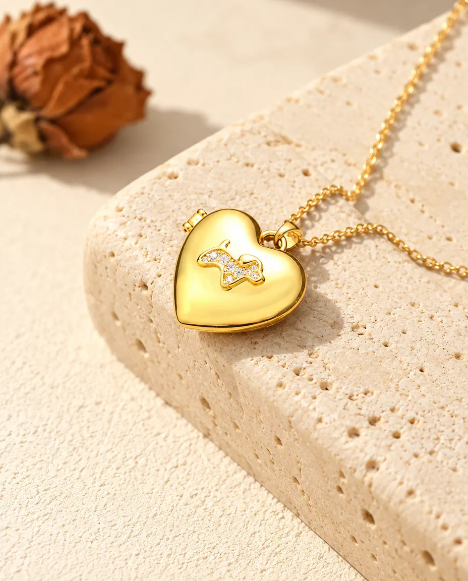 Collar relicario de corazón dorado con perrito, apoyado en un bloque de travertino