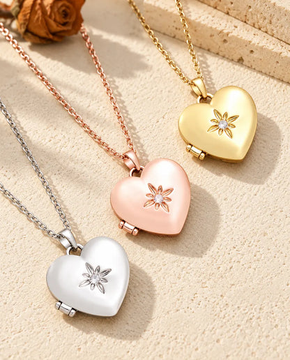 Relicarios de corazón satinados con flor en plateado, color oro rosa y dorado, colocados en diagonal sobre yeso crema