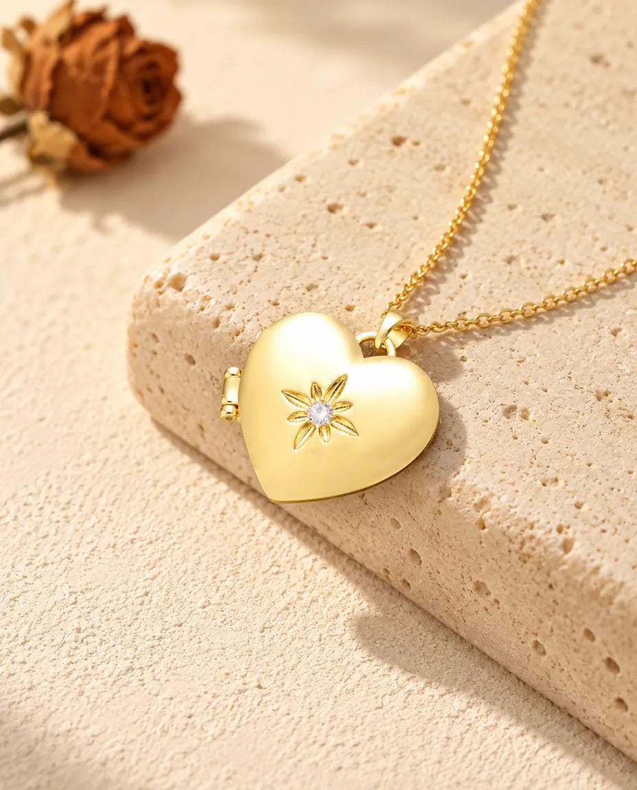 Collar relicario de corazón dorado satinado con flor, apoyado en un bloque de travertino