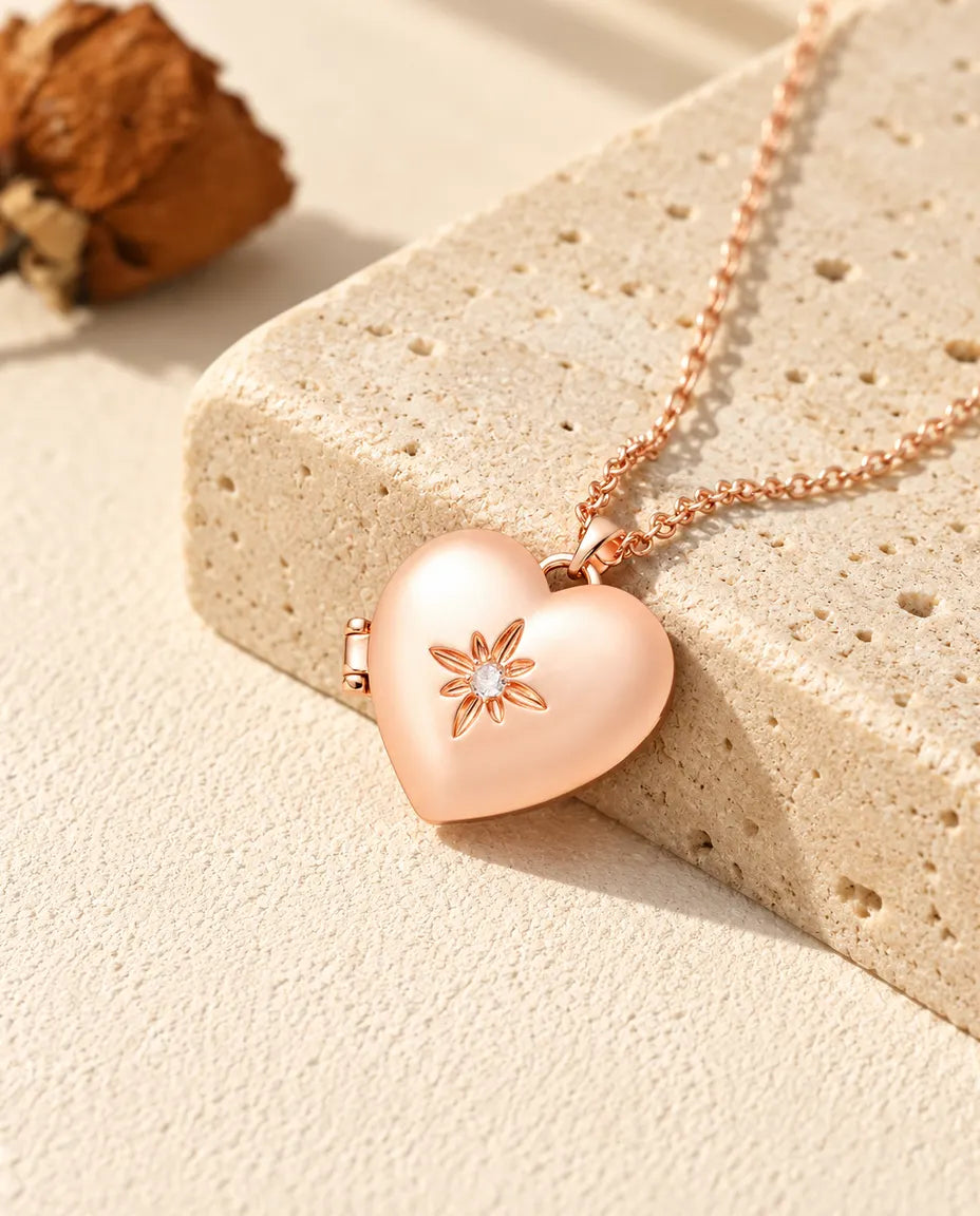 Collar relicario de corazón satinado con flor en color oro rosa sobre travertino, con luz cálida de sol