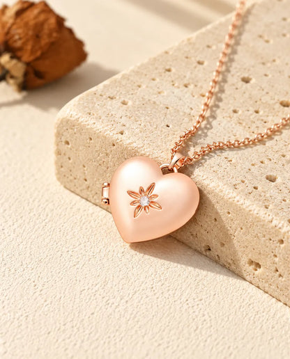 Collar relicario de corazón satinado con flor en color oro rosa sobre travertino, con luz cálida de sol