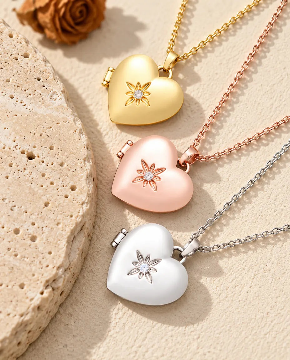 Relicarios de corazón satinados con flor dorado, color oro rosa y plateado apilados junto a una losa de travertino
