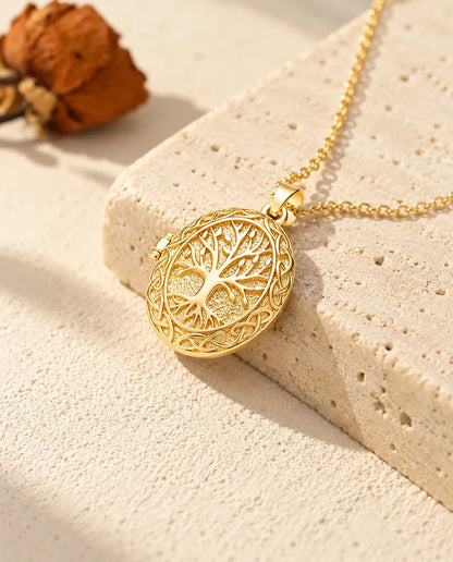 Collar relicario ovalado dorado con árbol de la vida colgado sobre el borde de un bloque de travertino