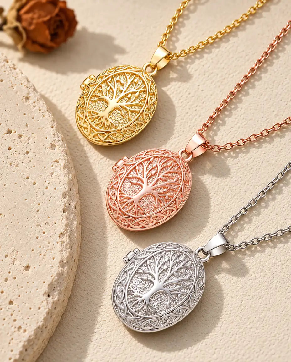 Relicarios con árbol de la vida dorado, color oro rosa y plateado apilados junto a una losa de travertino