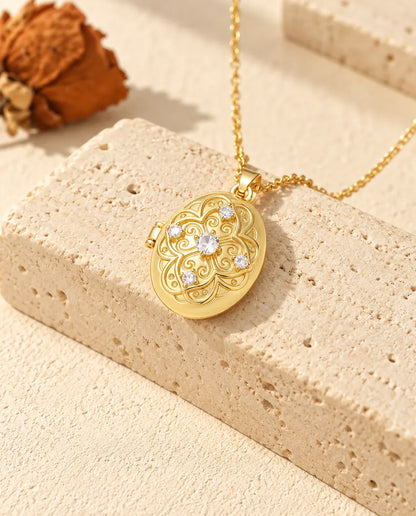 Collar relicario ovalado de filigrana en dorado, con la cadena cayendo sobre un bloque de travertino