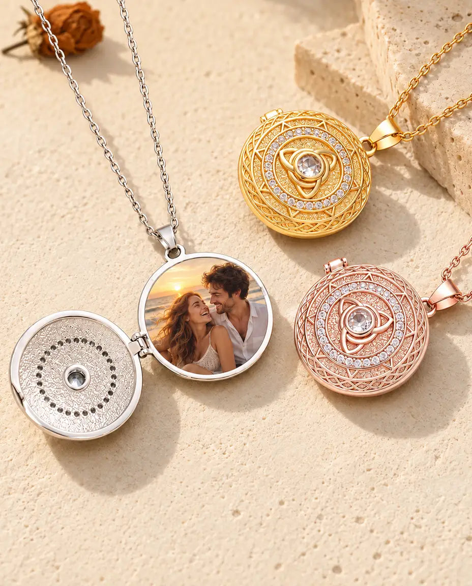 Relicario plateado abierto con una foto de una pareja en la playa, junto a dos relicarios cerrados dorado y color oro rosa