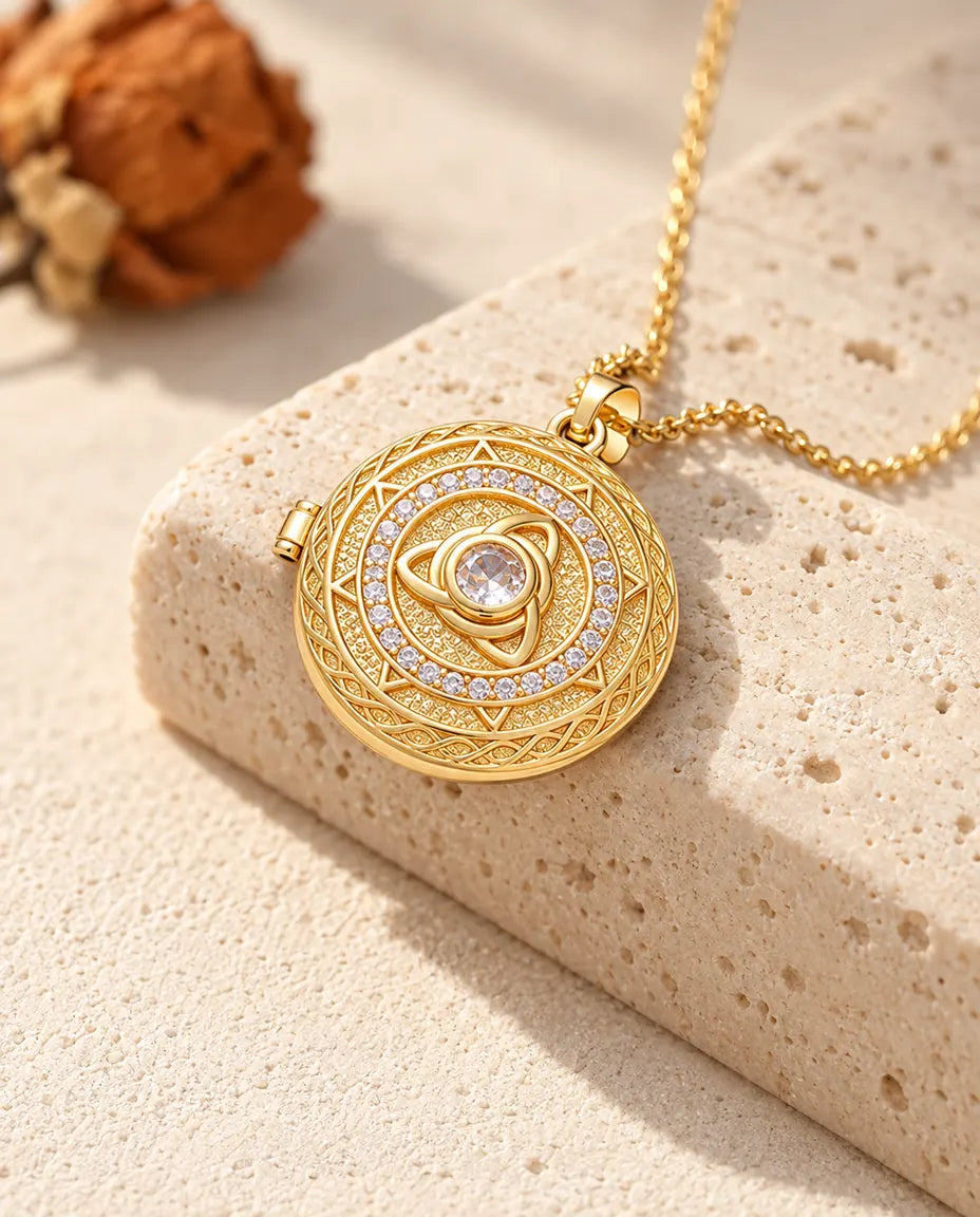 Collar relicario redondo dorado con triqueta y circonita central colgado sobre un bloque de travertino