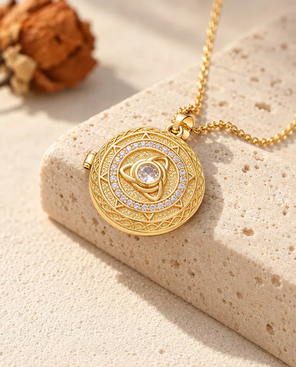 Collar relicario redondo dorado con triqueta y circonita central colgado sobre un bloque de travertino