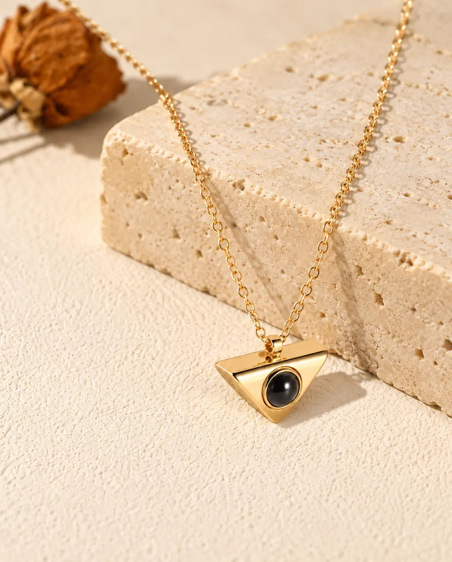 Collar de triángulo dorado con foto dentro, colgado sobre un bloque de travertino