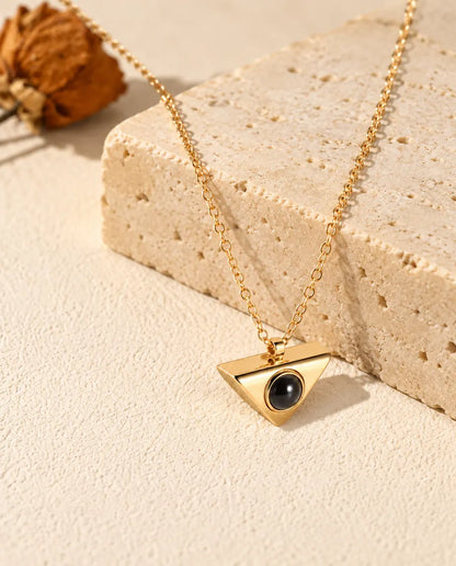 Collar de triángulo dorado con foto dentro, colgado sobre un bloque de travertino