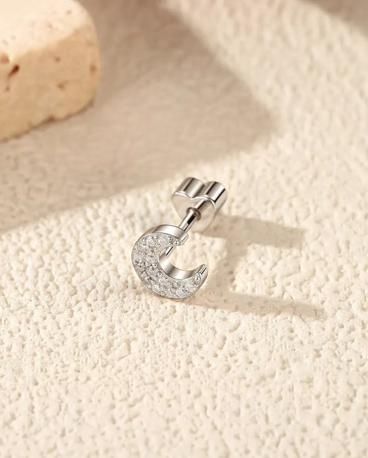 Pendientes Luna Creciente Pavé de Moissanita en Plata 925 - tumbado de lado sobre una superficie clara con textura, con el cierre en forma de corazón en el poste
