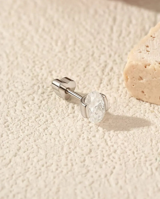 Pendientes de Moissanita Oval con Engaste Lateral en Plata 925 - tumbado de lado sobre una superficie clara con textura, con el cierre en forma de corazón en el poste