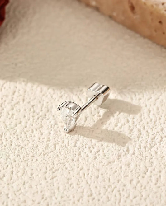 Pendientes de Moissanita Talla Pera con Dos Garras en Plata 925 - tumbado de lado sobre una superficie clara con textura, con el cierre en forma de corazón en el poste