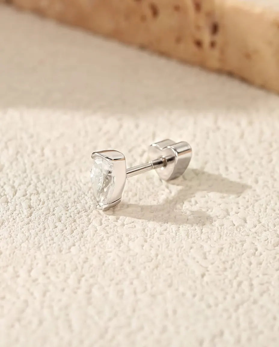 Pendientes de Moissanita Talla Pera en Plata 925 - sobre una superficie clara con textura junto a una losa de travertino