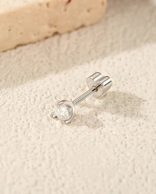 Pendientes de Moissanita Redonda con Arco Lateral en Plata 925 - tumbado de lado sobre una superficie clara con textura, con el cierre en forma de corazón en el poste