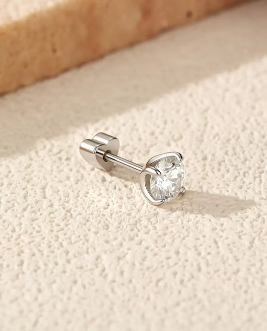 Pendientes Solitario de Moissanita de 5 mm con Cuatro Garras en Plata 925 - tumbado de lado sobre una superficie clara con textura, con el cierre en forma de corazón en el poste