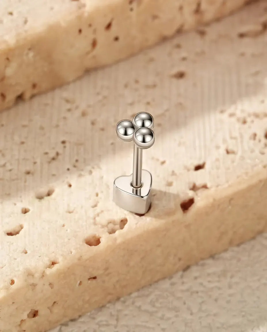 Pendientes Trébol de Tres Bolitas en Plata 925 - de pie sobre su cierre en forma de corazón, en una superficie clara con textura