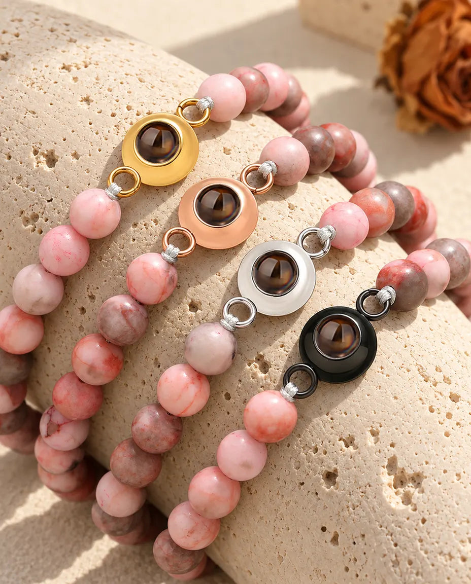 Pulseras de bolas rosa moteado con cada color de aro, alineadas sobre travertino