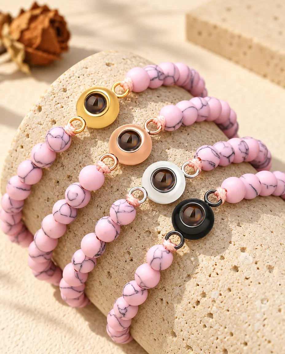 Pulseras de bolas rosa jaspeado con los cuatro colores de aro, colocadas sobre travertino