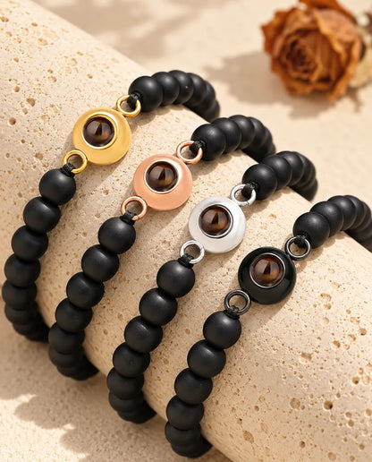 Pulseras de bolas negro mate con cada color de aro, colocadas sobre un bloque de travertino