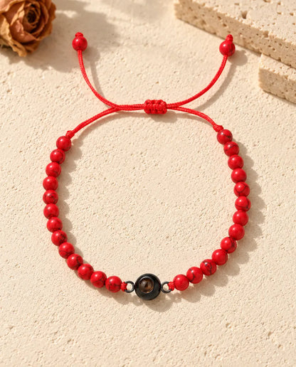 Vista cenital de la pulsera de bolas rojas con aro negro de proyección y nudo corredizo