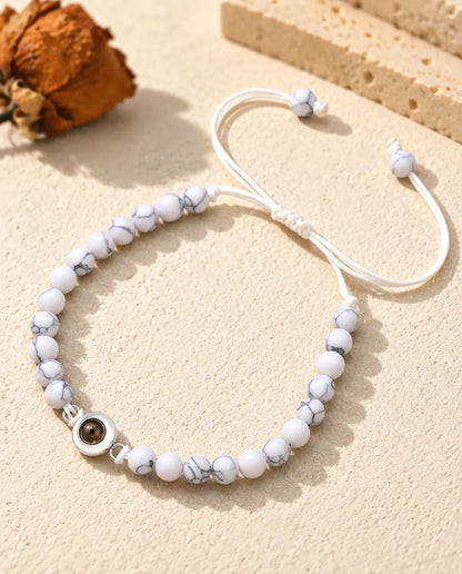 Pulsera de bolas blanco jaspeado con aro de proyección plateado y nudo corredizo