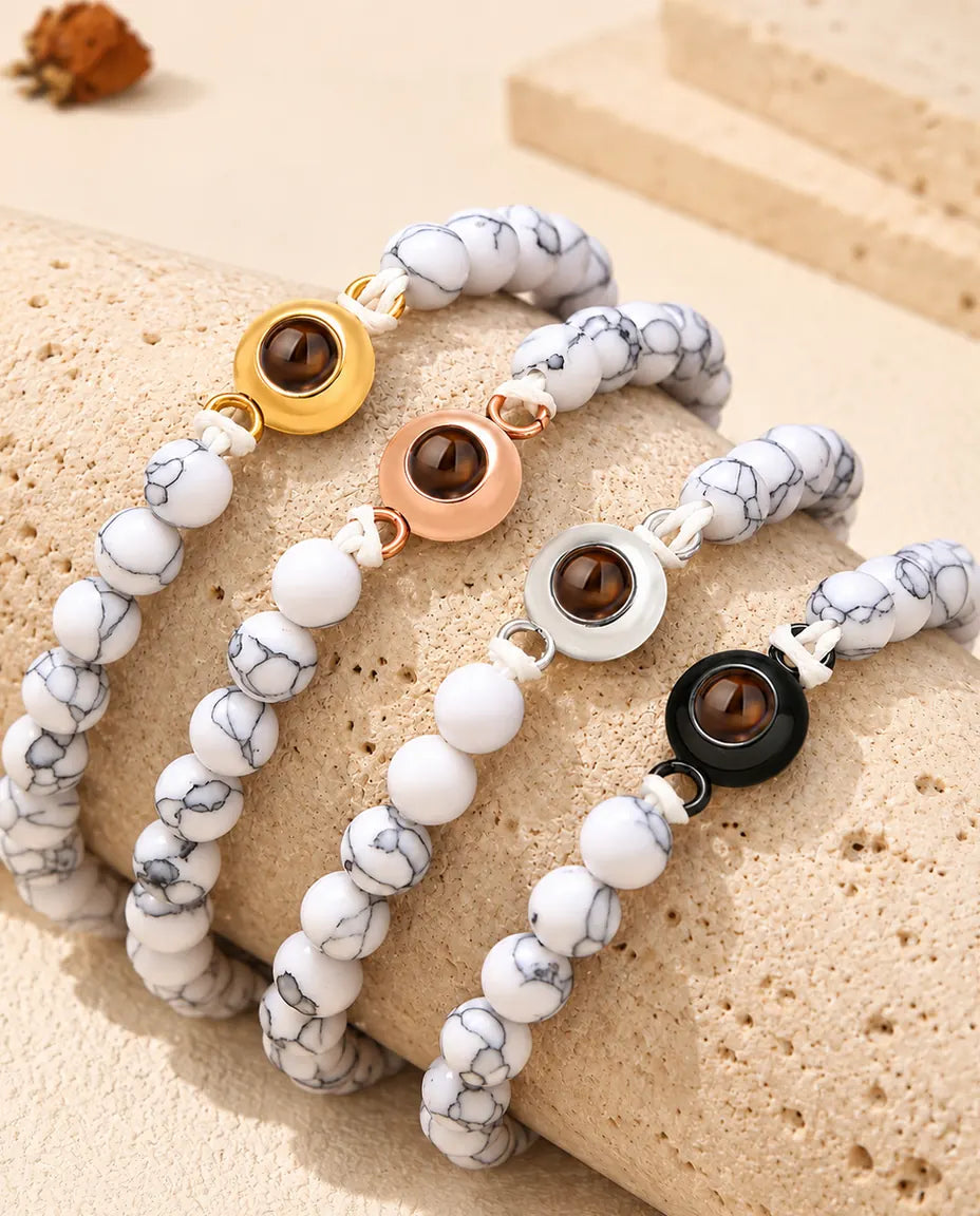 Pulseras de bolas blanco jaspeado con cada color de aro, colocadas sobre un bloque de travertino