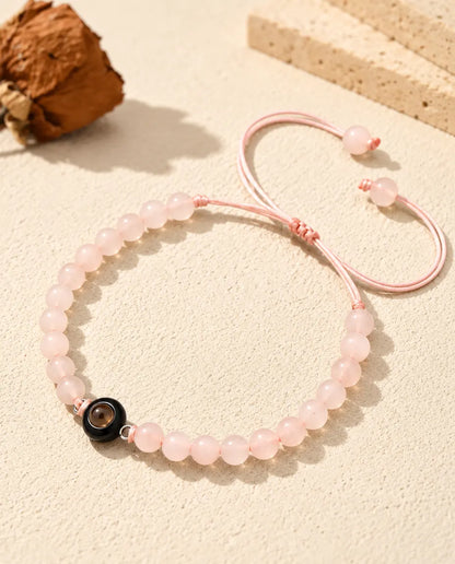 Pulsera de bolas rosa palo con aro de proyección negro, apoyada sobre yeso color crema