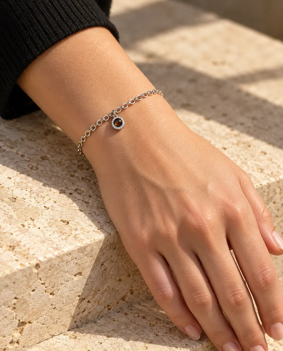 Mujer con la pulsera plateada de colgante redondo de circonitas en la muñeca, bajo una cálida luz de sol