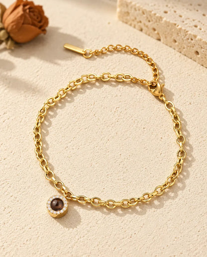 Pulsera dorada con foto dentro y colgante redondo de circonitas, apoyada sobre yeso color crema