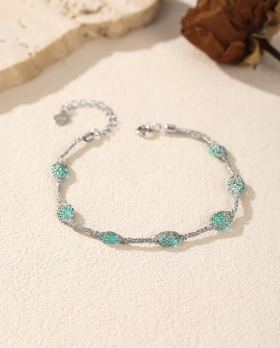 Pulsera de Circonitas en Jaula en Plata 925 - versión con circonitas verdes junto a una losa de travertino y una rosa seca