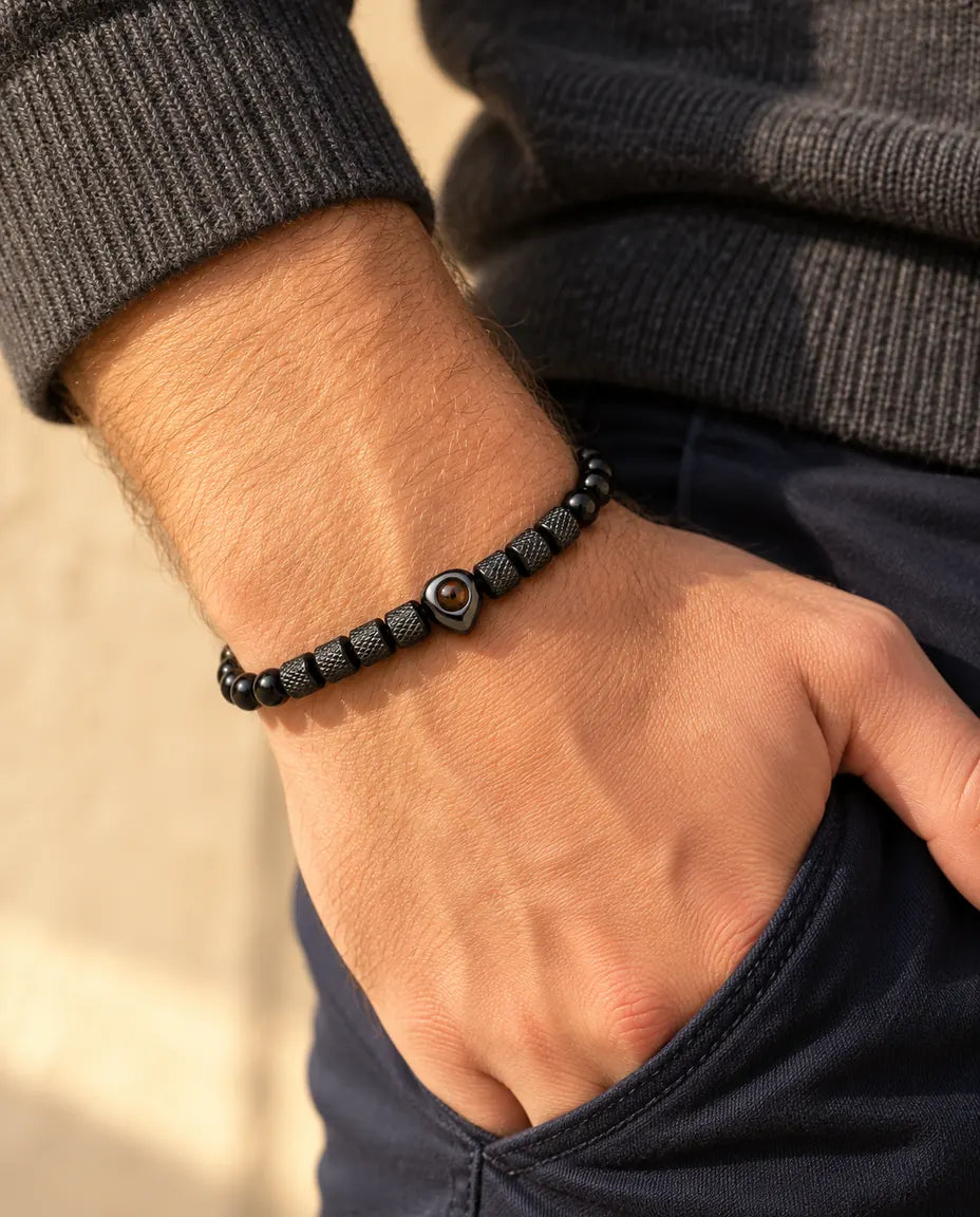Hombre con la pulsera negra de cuentas con corazón y foto dentro, con el pulgar en el bolsillo