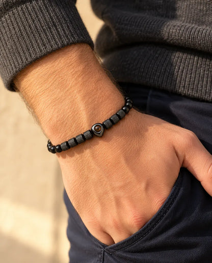 Hombre con la pulsera negra de cuentas con corazón y foto dentro, con el pulgar en el bolsillo