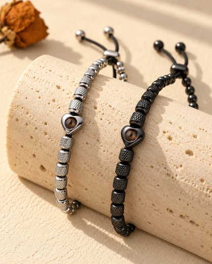 Pulseras de cuentas con corazón en plateado y negro colgando sobre un bloque de travertino