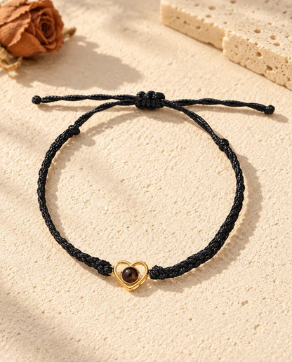 Vista cenital de la pulsera de corazón abierto dorado en cordón trenzado negro, con el nudo corredizo