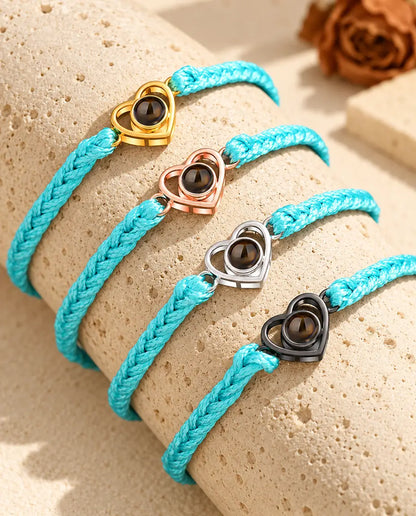 Cuatro pulseras de cordón trenzado azul con corazón abierto dorado, color oro rosa, de plata y negro sobre travertino
